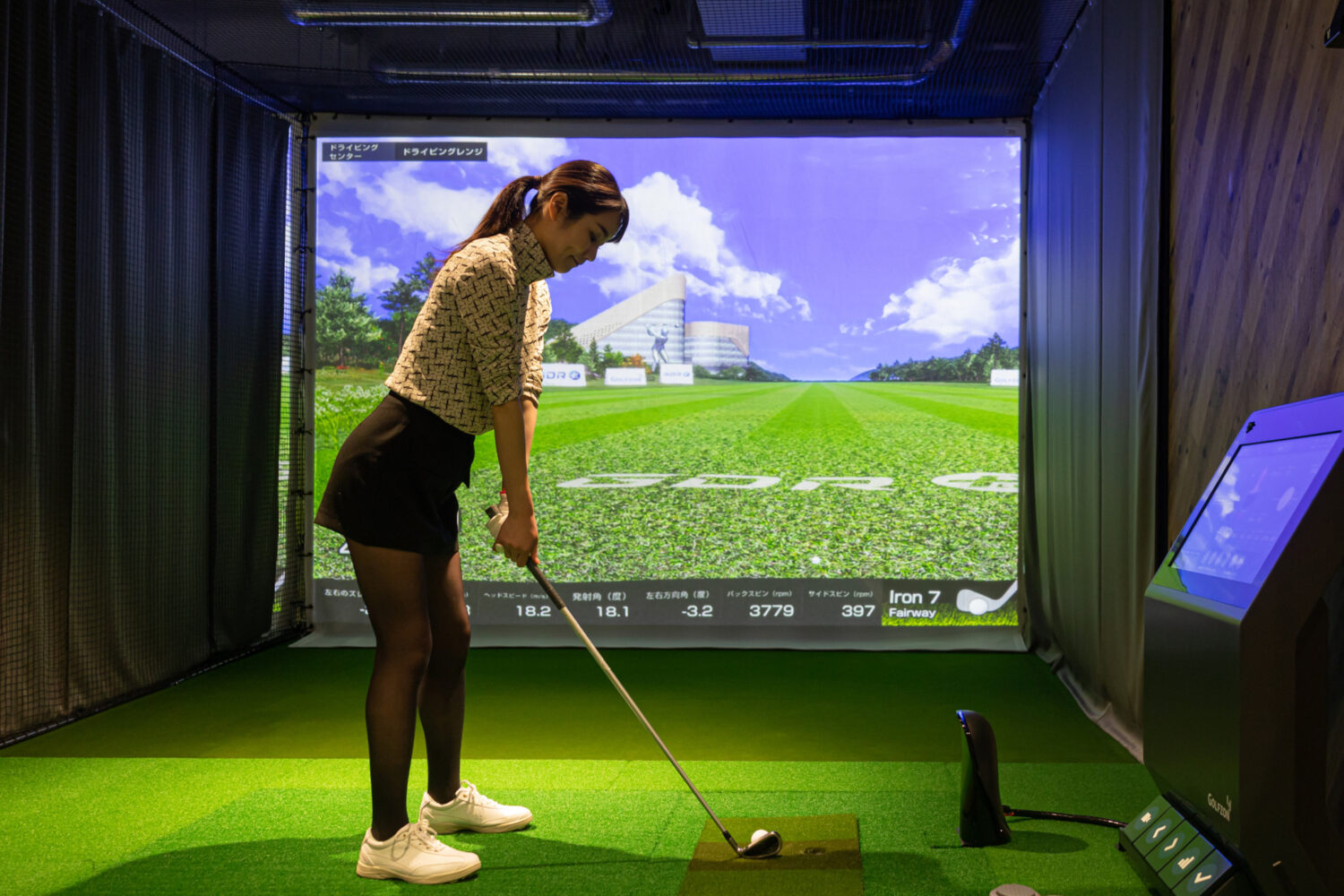 インドアゴルフ練習場でシミュレーションゴルフを利用する女性